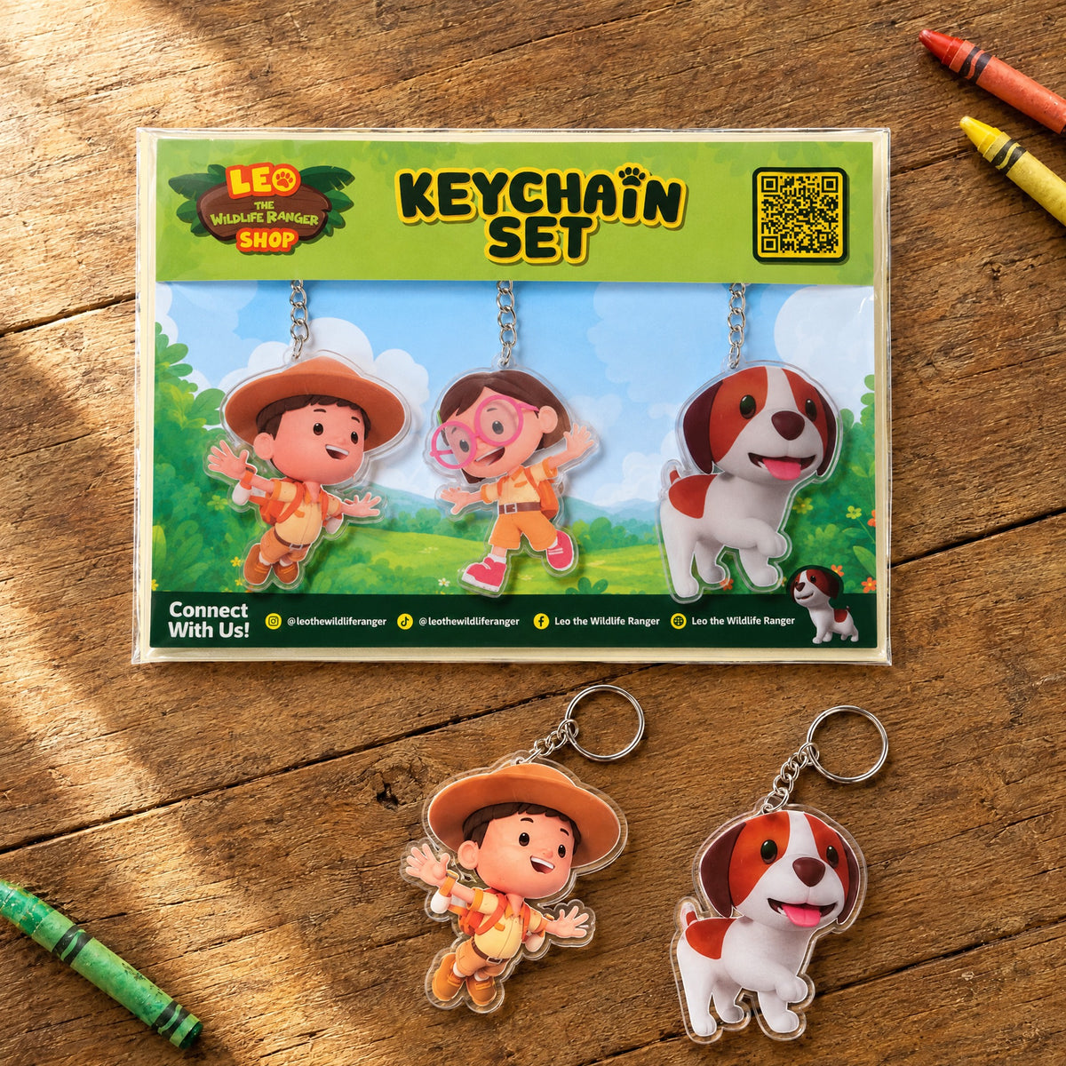 Leo The Wildlife Ranger acrylic keychain set of 3 (Leo, Katie, Hero) on a wooden table with crayons